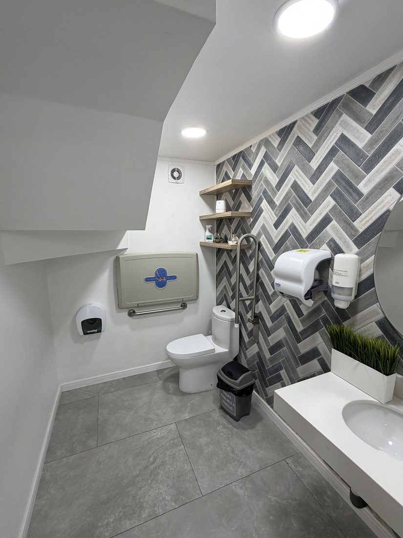 Baño de pacientes con lavamanos, dispensadores de jabón y papel, y espejo redondo