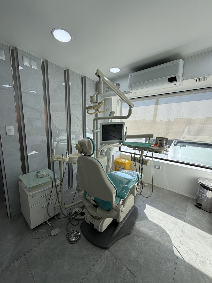 Sillón dental equipado con bandeja de instrumental y lámpara, junto a la ventana del box